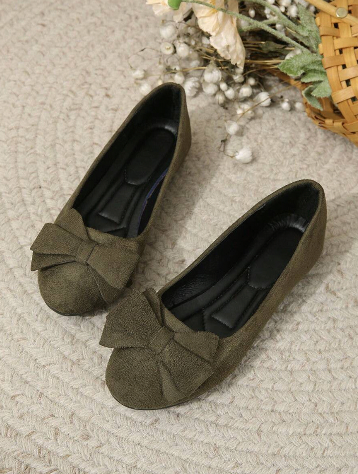 Elegant women's flats with a bow design, crafted for comfort and style, displayed on a textured surface with decorative floral accents nearby.