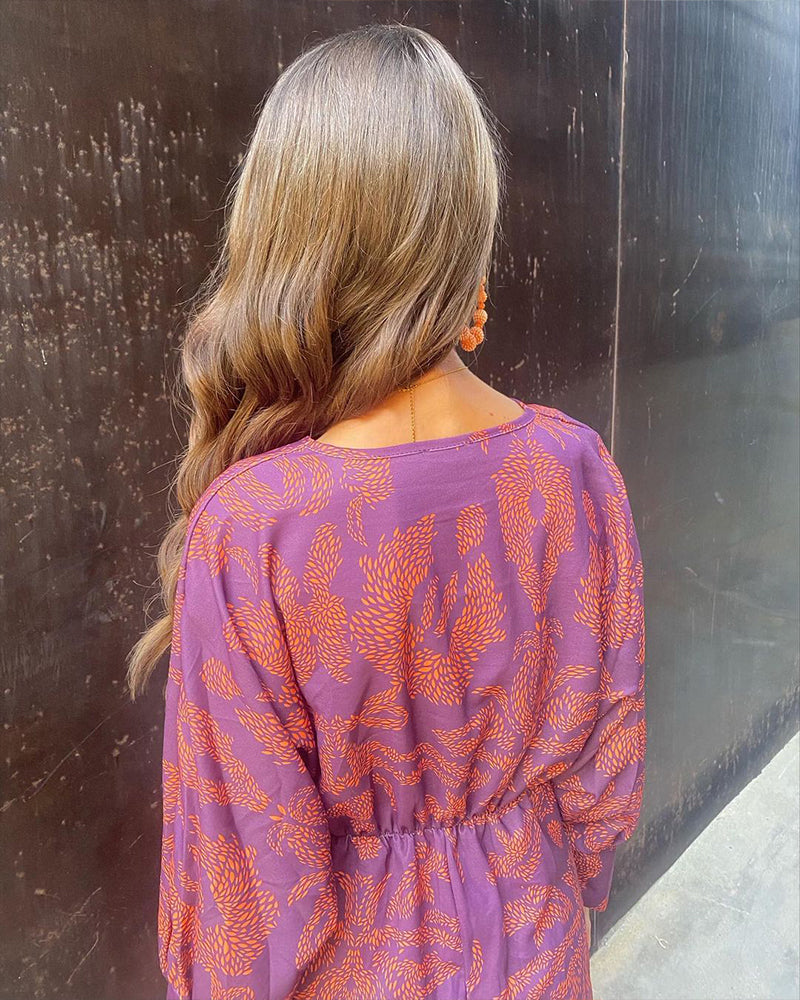 A close-up of a woman wearing the Nina Women's Elegant Wrap Dress, featuring a bold pattern and flattering wrap design with a deep V-neckline. The dress showcases intricate patterns and a knot detail at the waist, creating a sophisticated and stylish look suitable for special occasions.