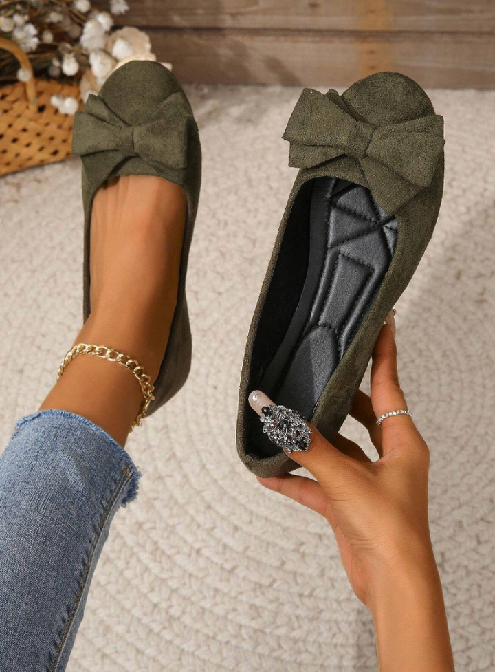 Elegant women's flats with a bow design, crafted for comfort and style, displayed on a textured surface with decorative floral accents nearby.