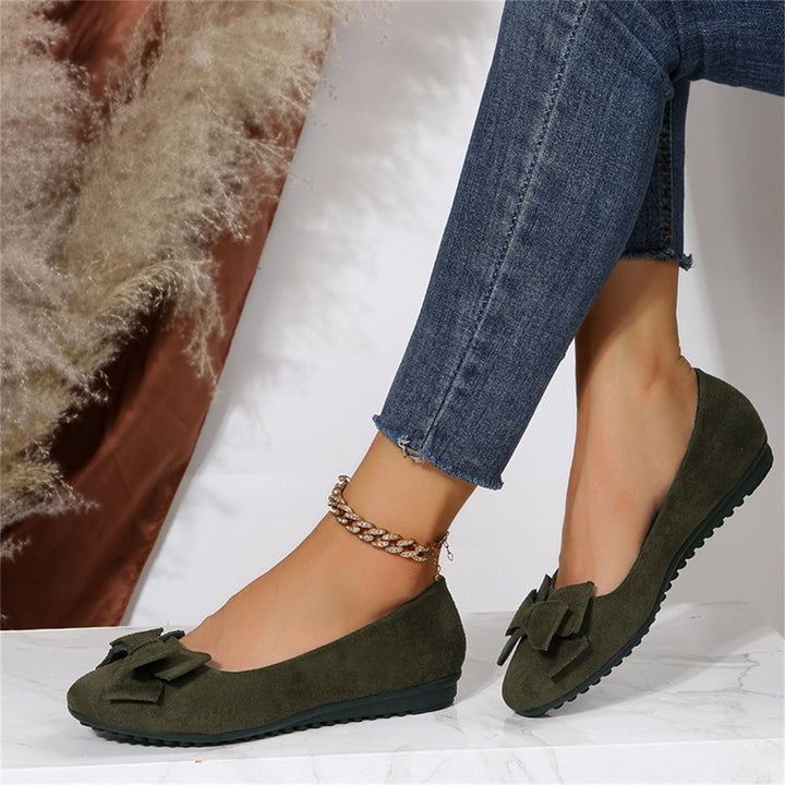 Elegant women's flats with a bow design, crafted for comfort and style, displayed on a textured surface with decorative floral accents nearby.