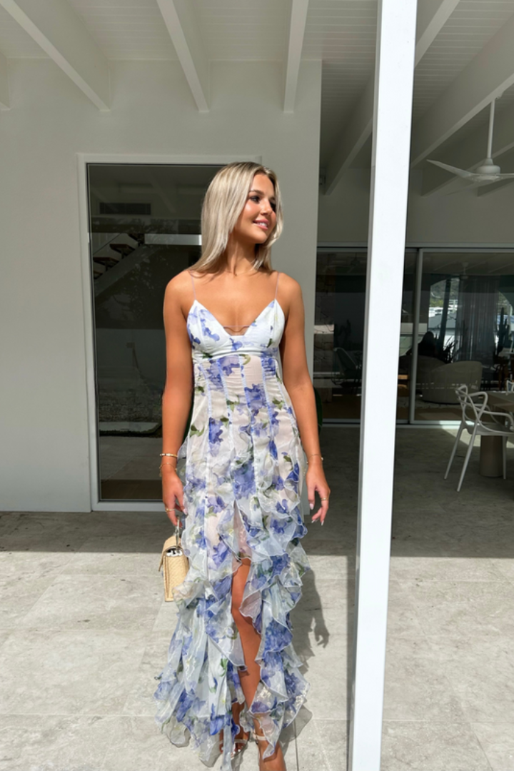 An elegant maxi dress featuring a ruffled design and a flattering silhouette, perfect for special occasions or evening wear. The model is styled on a scenic terrace, showcasing the sophisticated and graceful appeal of the dress.