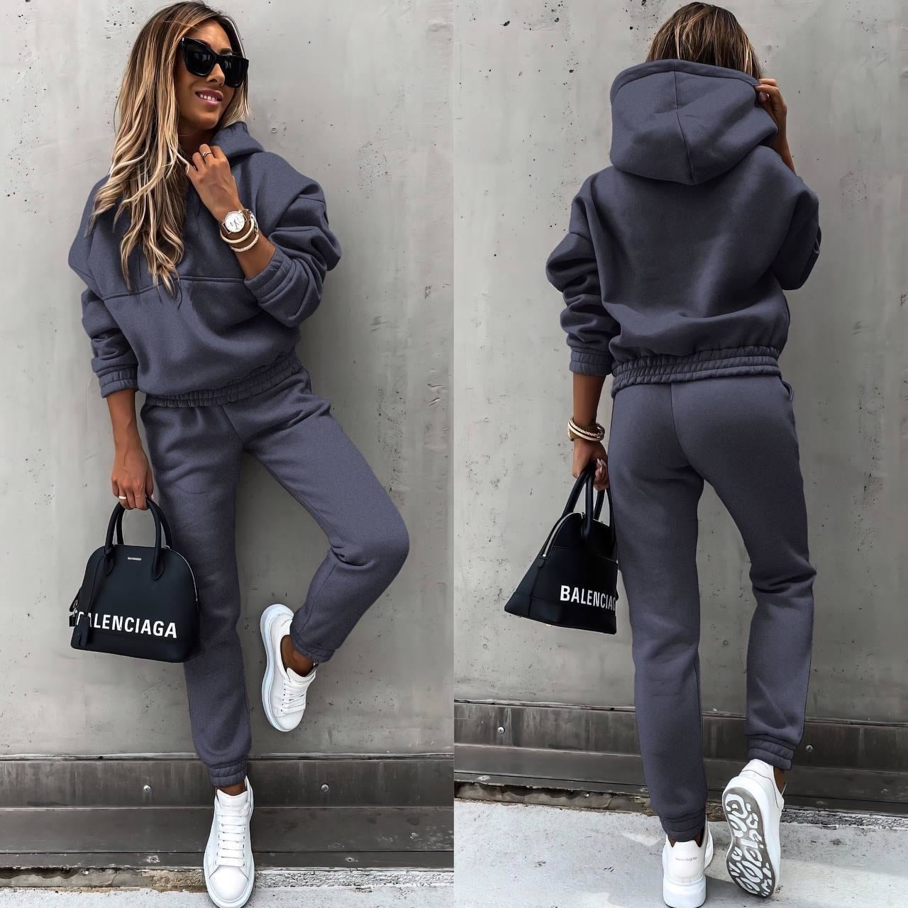 A woman wearing a casual two-piece tracksuit set with a hoodie and jogger-style pants. The outfit features a relaxed fit, perfect for both lounging and casual outings. She pairs it with white sneakers and a stylish handbag, creating a comfortable yet chic look.