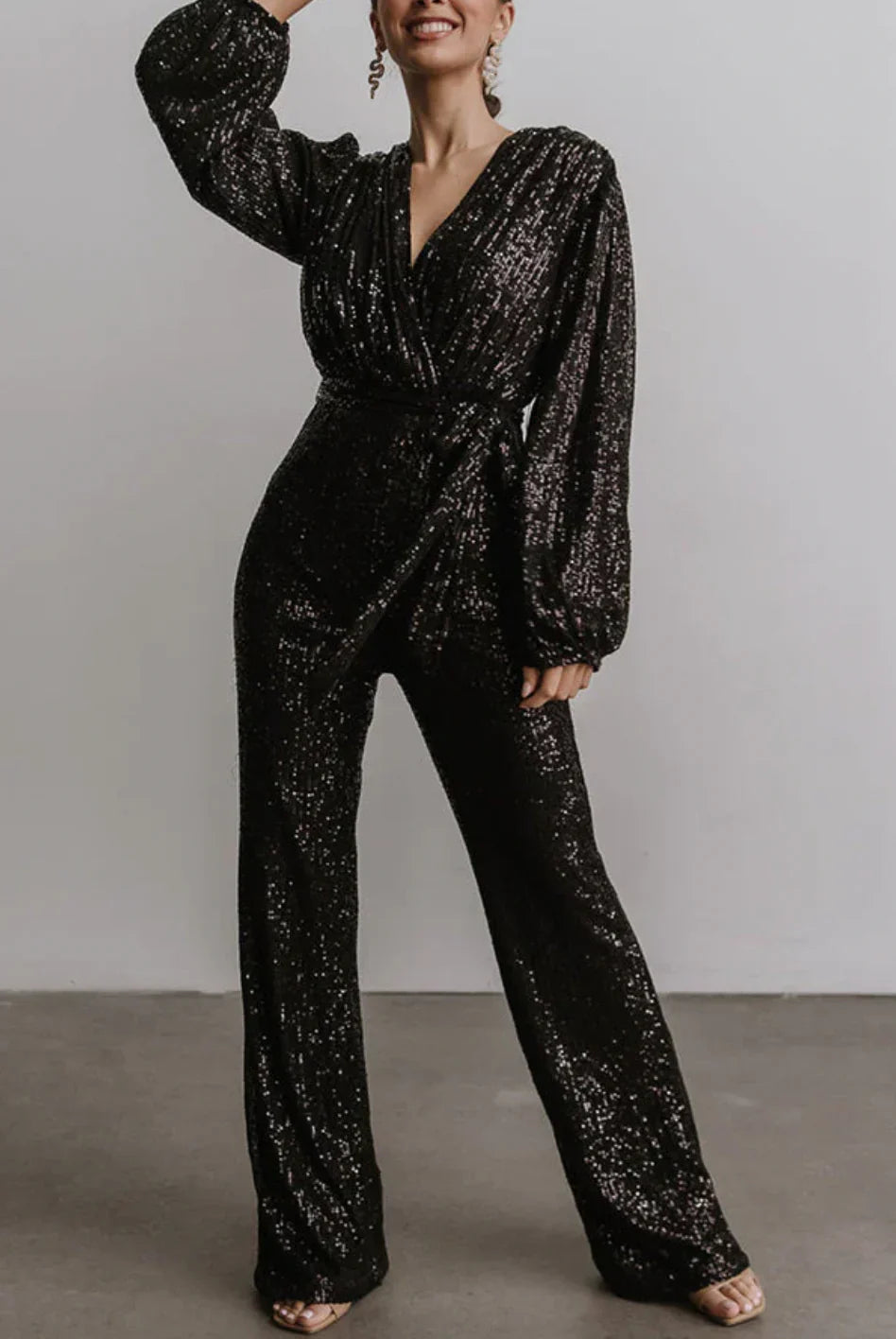 Model wearing the Isabella | Glamorous Sequin Jumpsuit, featuring a wrap-style top, long sleeves, and a wide-leg cut adorned with sparkling sequins. Perfect for special occasions, this jumpsuit combines elegance and comfort for a bold, statement-making look.