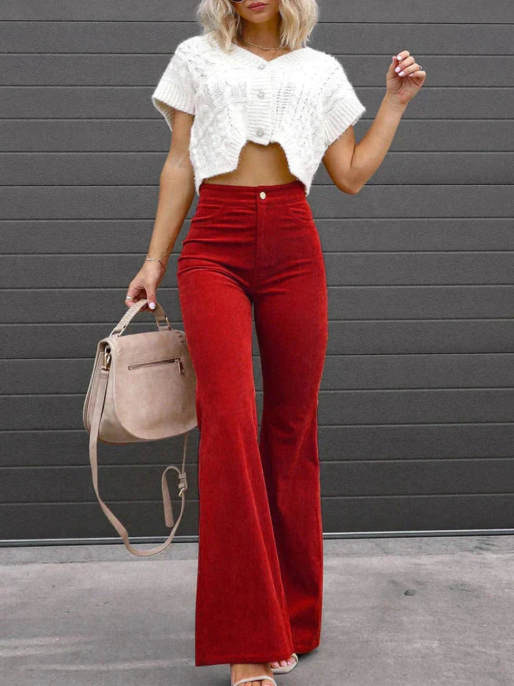 Full-body view of a woman wearing Harper high-waisted flare pants in a retro style, paired with a cropped top, holding a handbag, standing outdoors.