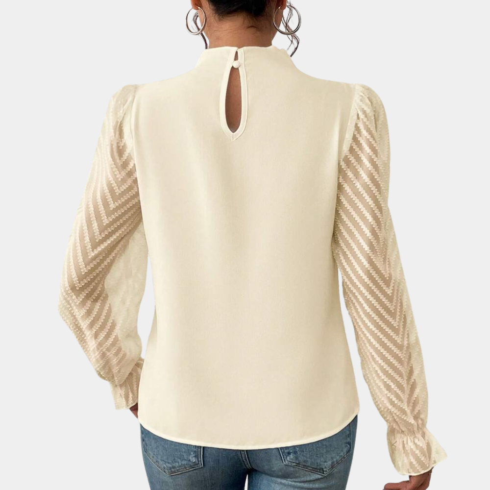 Woman wearing an elegant blouse with a high neckline, pleated front detail, sheer long sleeves with a subtle pattern, and ruffled cuffs, paired with denim jeans for a stylish and sophisticated look.