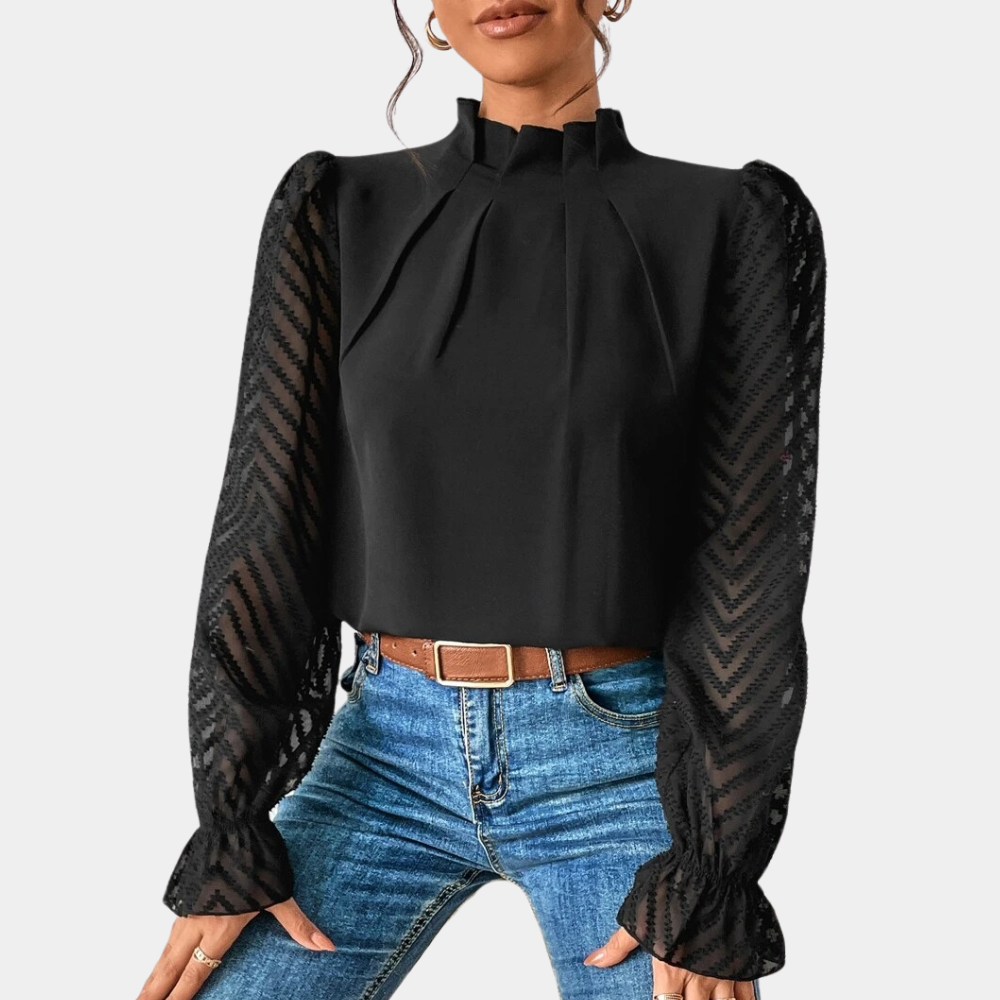 Woman wearing an elegant blouse with a high neckline, pleated front detail, sheer long sleeves with a subtle pattern, and ruffled cuffs, paired with denim jeans for a stylish and sophisticated look.