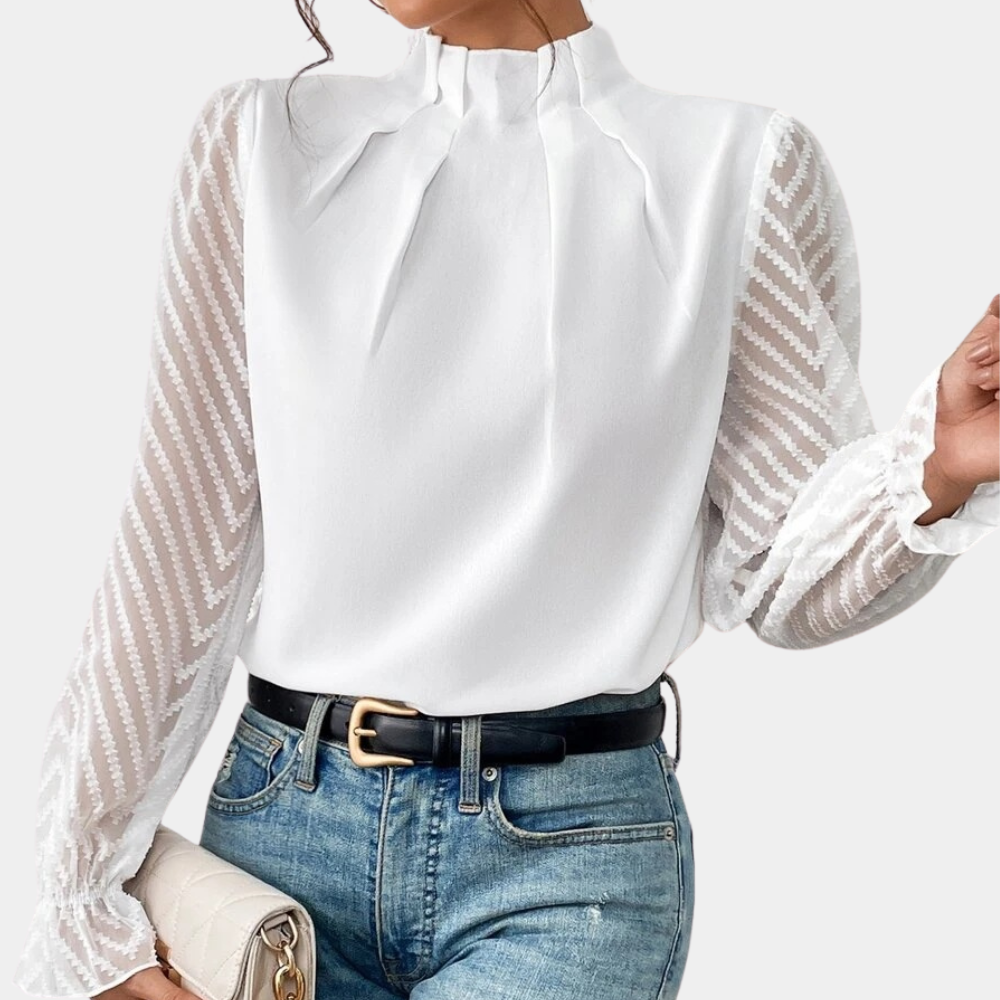 Woman wearing an elegant blouse with a high neckline, pleated front detail, sheer long sleeves with a subtle pattern, and ruffled cuffs, paired with denim jeans for a stylish and sophisticated look.