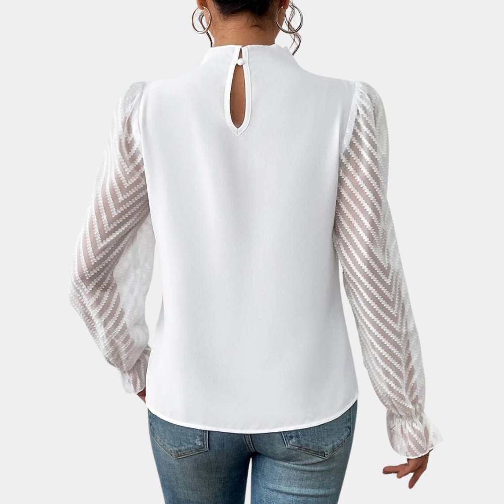 Woman wearing an elegant blouse with a high neckline, pleated front detail, sheer long sleeves with a subtle pattern, and ruffled cuffs, paired with denim jeans for a stylish and sophisticated look.