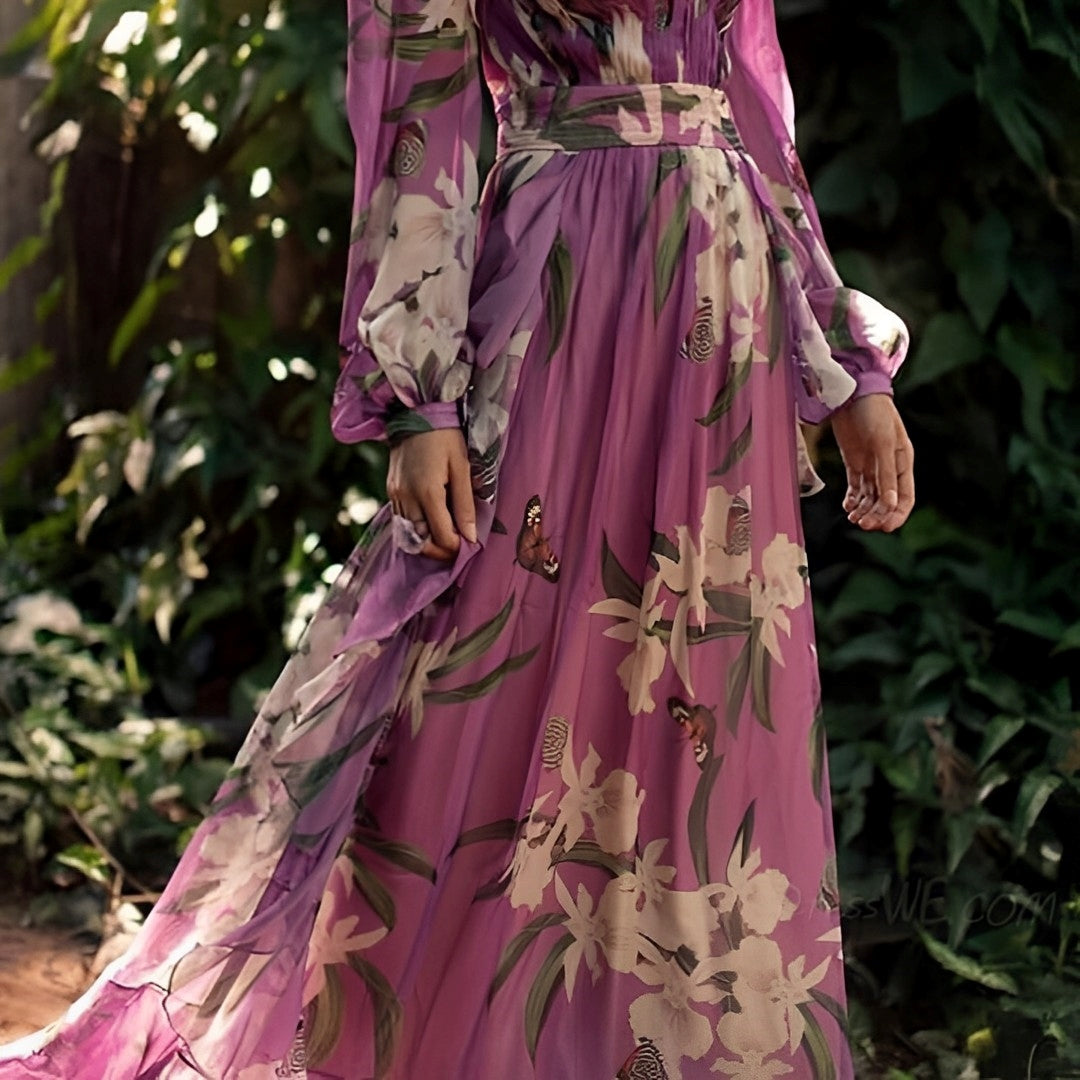 Woman wearing the Elara Women's Floral Chiffon Dress, an elegant long dress with a delicate floral design, flowy long sleeves, and a fitted waist, posing gracefully outdoors amidst lush greenery.