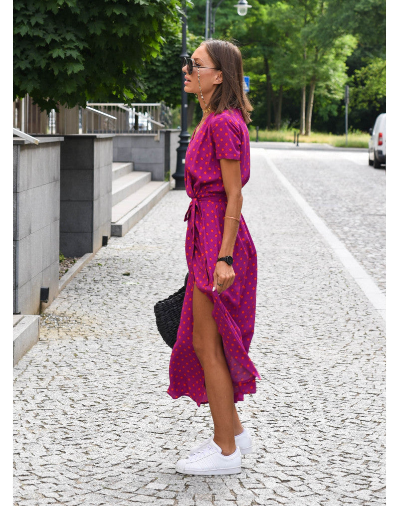 A woman walking down a street wearing the Lana Women's Elegant Wrap Dress, a casual midi dress with a flattering wrap design and tie waist, styled with sneakers and a woven handbag. This versatile dress is ideal for both casual outings and stylish gatherings.