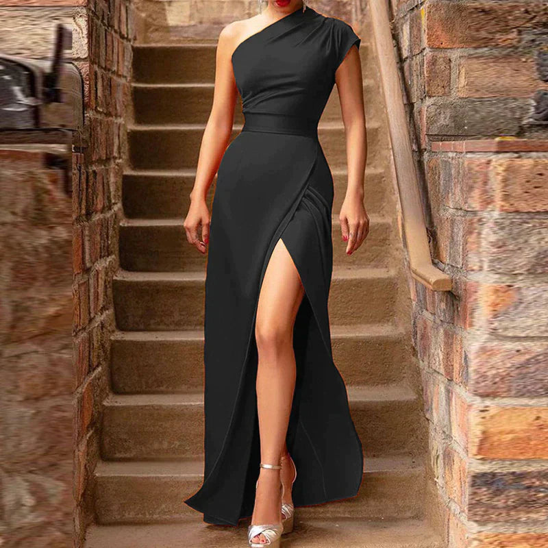 A woman wearing a one-shoulder evening gown with a fitted silhouette and a high side slit, posing elegantly in an outdoor setting. The gown has a sleek, sophisticated design, perfect for formal events or special occasions.