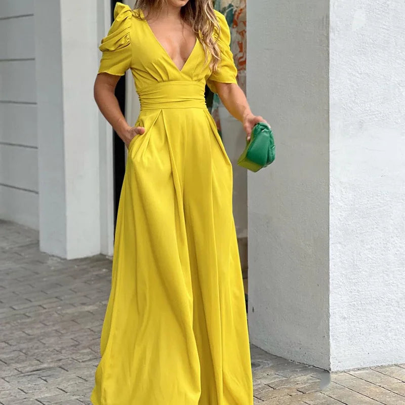 Woman wearing the Vivian Women's Puff Sleeve Maxi Dress, a V-neck dress with elegant puff sleeves and a flowing maxi silhouette, holding a small clutch bag and standing stylishly on a paved walkway.