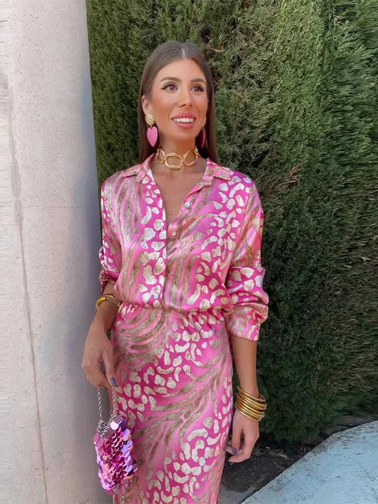 Woman wearing the Sofia Women's Satin Button-Up Dress, a luxurious dress with a bold, intricate print, styled with statement jewelry and a small textured handbag, posing elegantly outdoors against a lush green background.