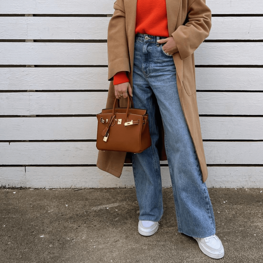 Image showing a woman holding an elegant handbag with a sleek design, featuring gold hardware and a structured shape, paired with casual attire for a stylish, sophisticated look.