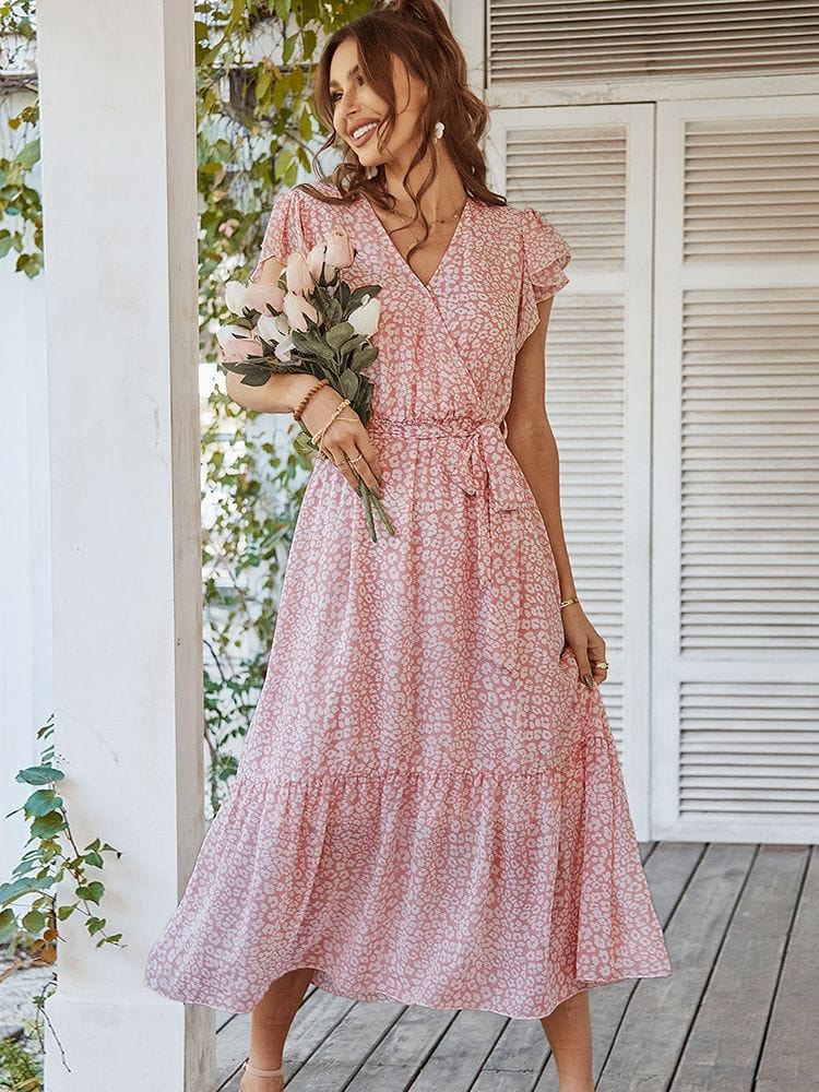 Woman wearing the Lily Women's Ruffle Wrap Dress, a midi dress with a flattering wrap design and ruffle details, standing on a wooden porch holding a small bouquet, exuding a soft, romantic look amidst a natural, floral setting.