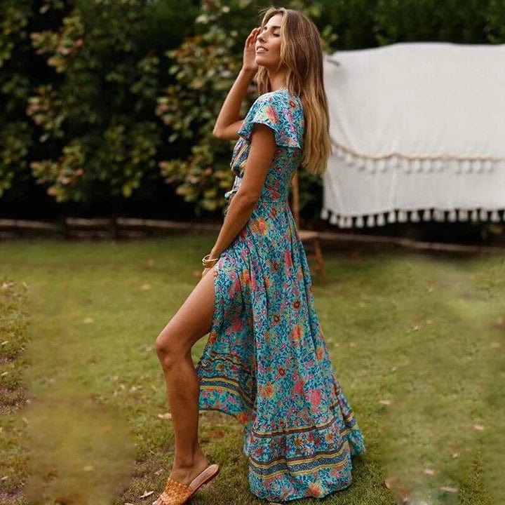 Full-length floral maxi dress with a flowing silhouette, flutter sleeves, and bohemian-inspired patterns, worn by a woman outdoors in a natural garden setting, capturing a sense of carefree elegance and movement.