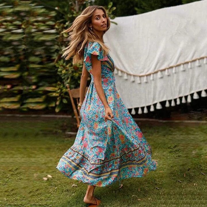 Full-length floral maxi dress with a flowing silhouette, flutter sleeves, and bohemian-inspired patterns, worn by a woman outdoors in a natural garden setting, capturing a sense of carefree elegance and movement.