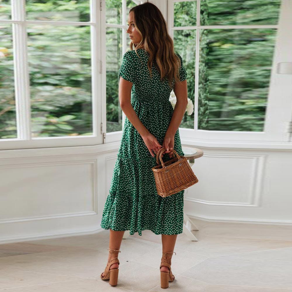 Woman wearing the Lily Women's Floral Midi Dress, a casual dress with a flowy, relaxed fit and delicate floral pattern, holding a woven handbag and posing elegantly indoors near a table decorated with flowers.