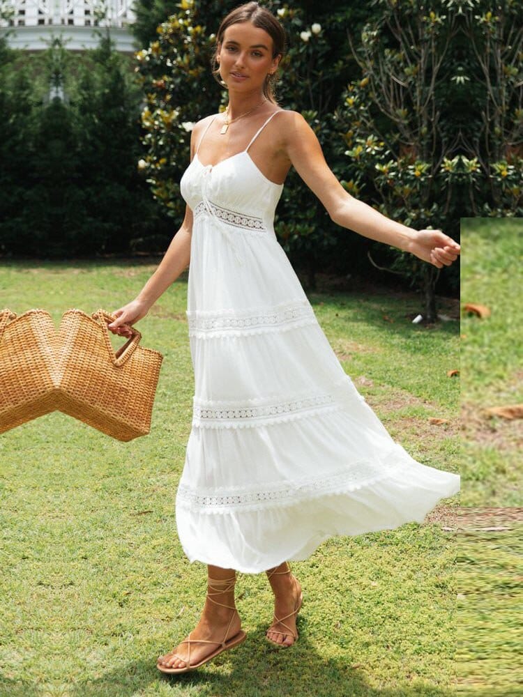 A woman walking in a garden wearing the Olivia | Strappy Tiered Midi Dress, featuring a flowy, tiered design with delicate straps. She holds a woven handbag, creating a chic, summery look perfect for outdoor occasions.