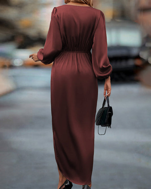 A woman wearing a long wrap dress with elegant long sleeves, walking confidently on a city street. The dress features a flattering wrap design that cinches at the waist, creating a graceful silhouette perfect for both formal and casual occasions. She carries a stylish handbag to complete the look.