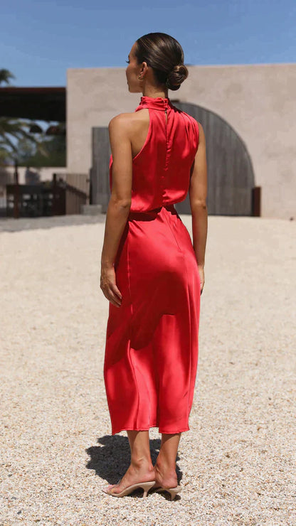 A woman wearing a sleeveless midi dress with an elegant draped neckline, standing outdoors in a stylish setting. The dress has a sleek and fitted silhouette, perfect for formal occasions or chic events. She is accessorized with minimalist heels for a polished, sophisticated look.