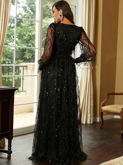 A woman wearing a stunning sequin gown with a deep V-neckline, sheer long sleeves, and a wrap design, posing elegantly indoors. The gown features a thigh-high slit and a belted waist, creating a glamorous and sophisticated look, perfect for formal events or special occasions.