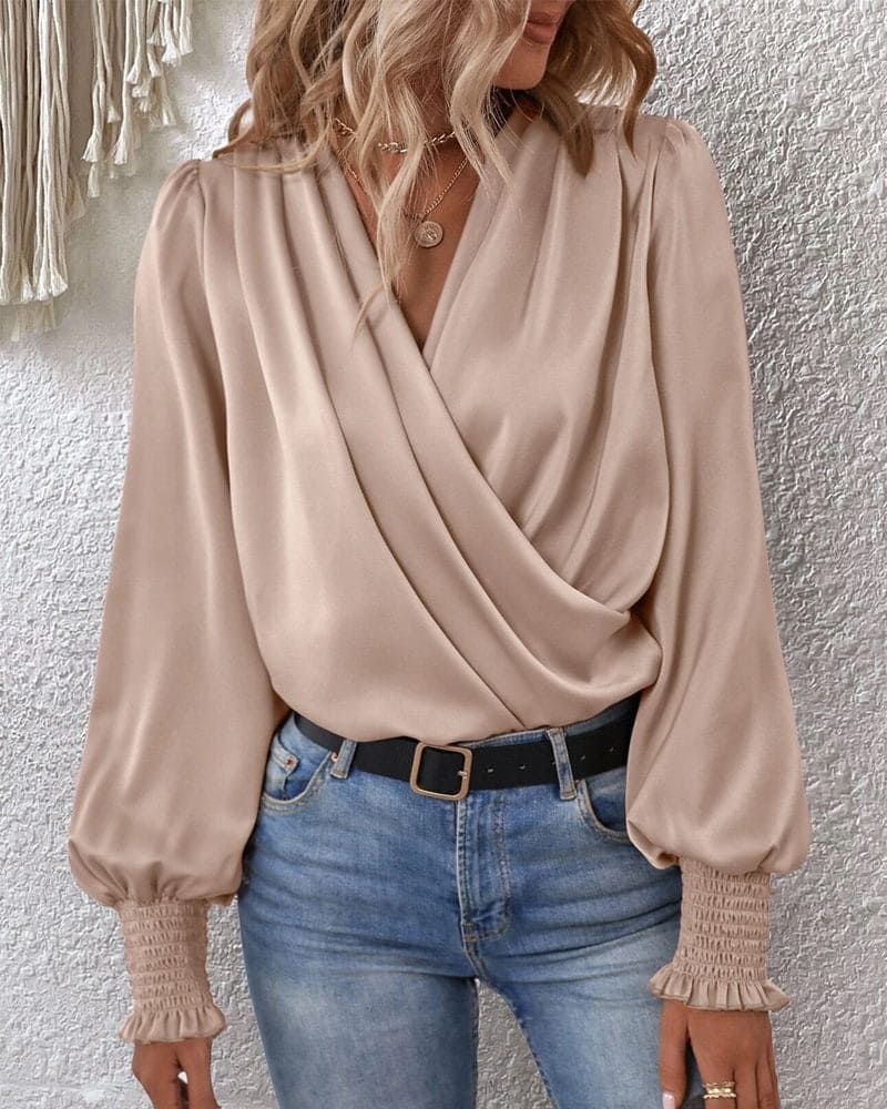 A woman wearing a stylish wrap blouse with long, billowy sleeves and smocked cuffs, tucked into high-waisted jeans. The blouse features a flattering draped front and a fitted waist, creating an elegant yet casual look perfect for both day and evening occasions.