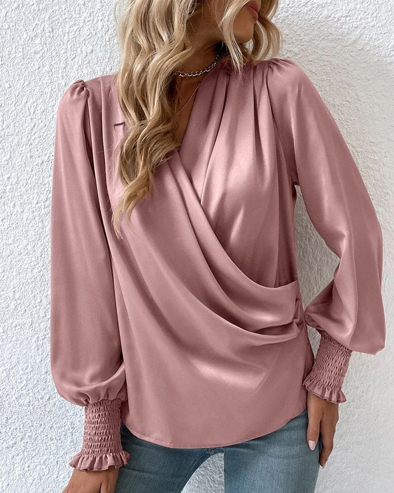 A woman wearing a stylish wrap blouse with long, billowy sleeves and smocked cuffs, tucked into high-waisted jeans. The blouse features a flattering draped front and a fitted waist, creating an elegant yet casual look perfect for both day and evening occasions.