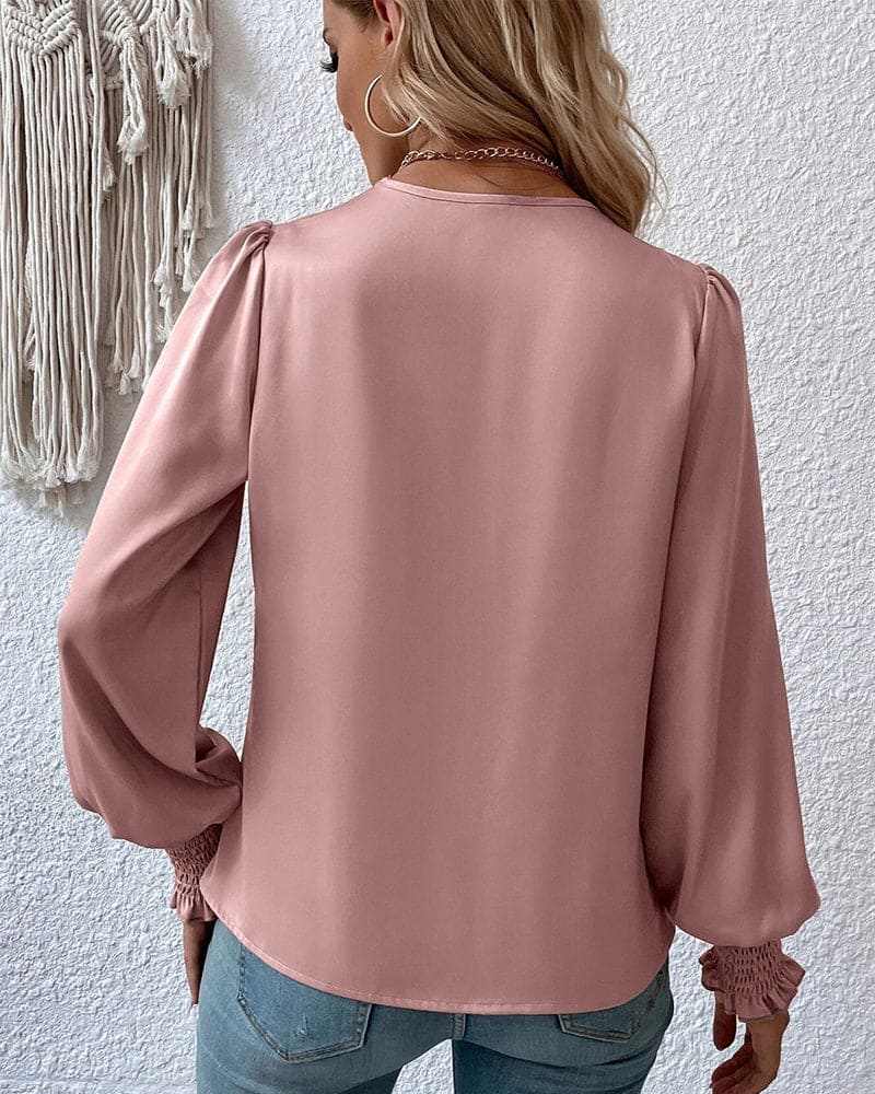 A woman wearing a stylish wrap blouse with long, billowy sleeves and smocked cuffs, tucked into high-waisted jeans. The blouse features a flattering draped front and a fitted waist, creating an elegant yet casual look perfect for both day and evening occasions.