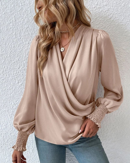 A woman wearing a stylish wrap blouse with long, billowy sleeves and smocked cuffs, tucked into high-waisted jeans. The blouse features a flattering draped front and a fitted waist, creating an elegant yet casual look perfect for both day and evening occasions.