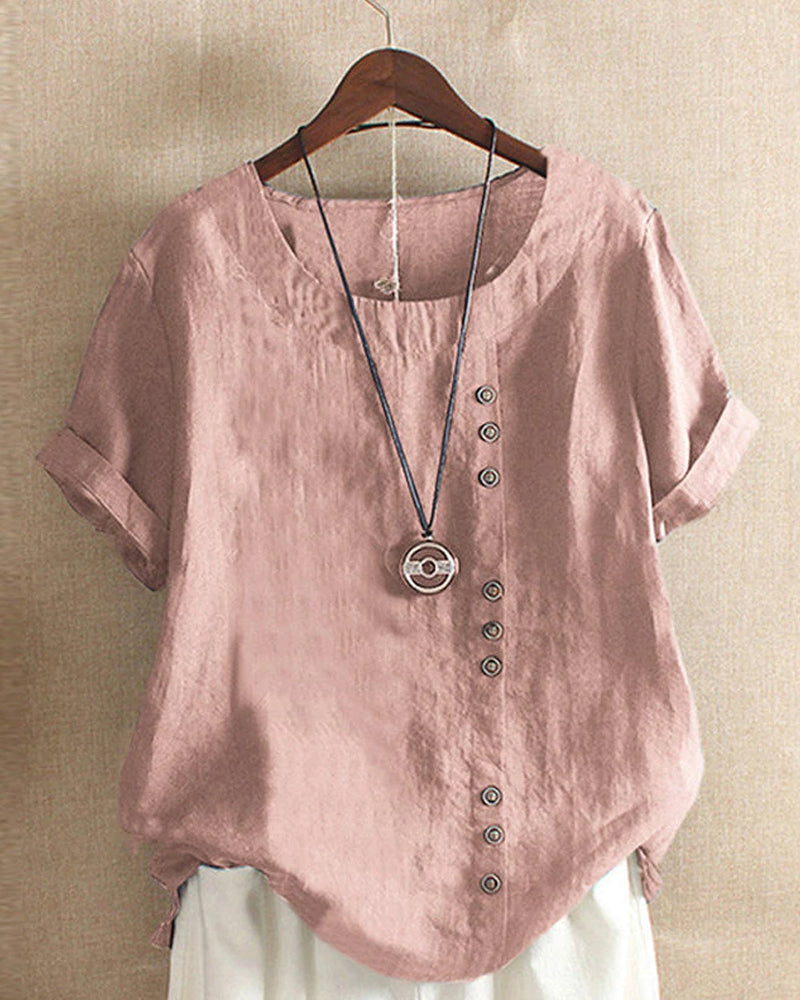 A casual women's blouse with an asymmetrical button design, short sleeves, and a relaxed fit, hanging on a wooden hanger. This blouse, part of the Mira collection, offers a unique style perfect for casual and everyday wear.