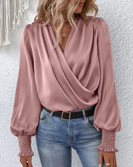 A woman wearing a stylish wrap blouse with long, billowy sleeves and smocked cuffs, tucked into high-waisted jeans. The blouse features a flattering draped front and a fitted waist, creating an elegant yet casual look perfect for both day and evening occasions.