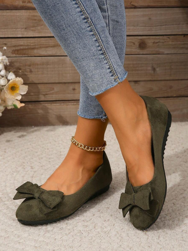  Elegant women's flats with a bow design, crafted for comfort and style, displayed on a textured surface with decorative floral accents nearby.