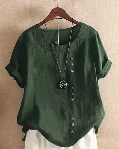 A casual women's blouse with an asymmetrical button design, short sleeves, and a relaxed fit, hanging on a wooden hanger. This blouse, part of the Mira collection, offers a unique style perfect for casual and everyday wear.