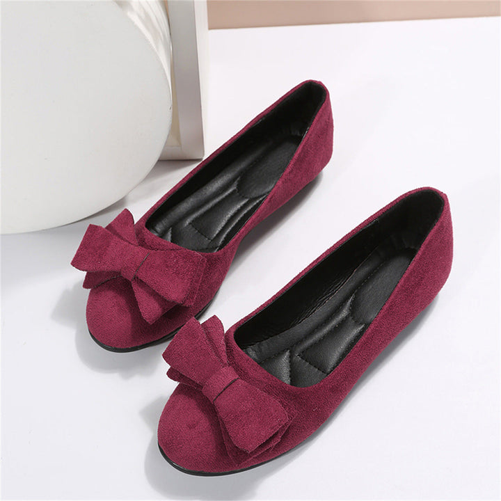  Elegant women's flats with a bow design, crafted for comfort and style, displayed on a textured surface with decorative floral accents nearby.