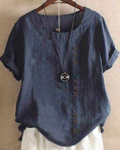 A casual women's blouse with an asymmetrical button design, short sleeves, and a relaxed fit, hanging on a wooden hanger. This blouse, part of the Mira collection, offers a unique style perfect for casual and everyday wear.