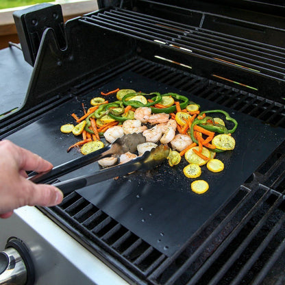 Non-stick grill mat placed on a barbecue grill with grilled salmon fillets and lemon slices, showcasing even cooking and ease of use.