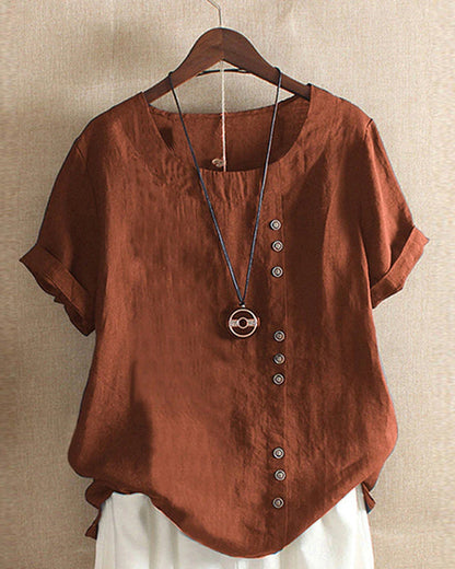 A casual women's blouse with an asymmetrical button design, short sleeves, and a relaxed fit, hanging on a wooden hanger. This blouse, part of the Mira collection, offers a unique style perfect for casual and everyday wear.