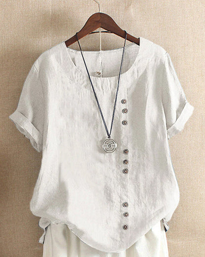 A casual women's blouse with an asymmetrical button design, short sleeves, and a relaxed fit, hanging on a wooden hanger. This blouse, part of the Mira collection, offers a unique style perfect for casual and everyday wear.