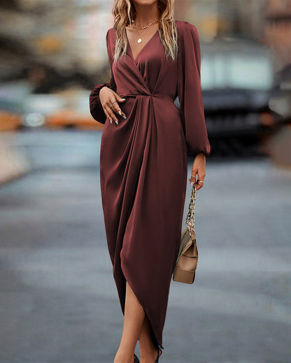 A woman wearing a long wrap dress with elegant long sleeves, walking confidently on a city street. The dress features a flattering wrap design that cinches at the waist, creating a graceful silhouette perfect for both formal and casual occasions. She carries a stylish handbag to complete the look.