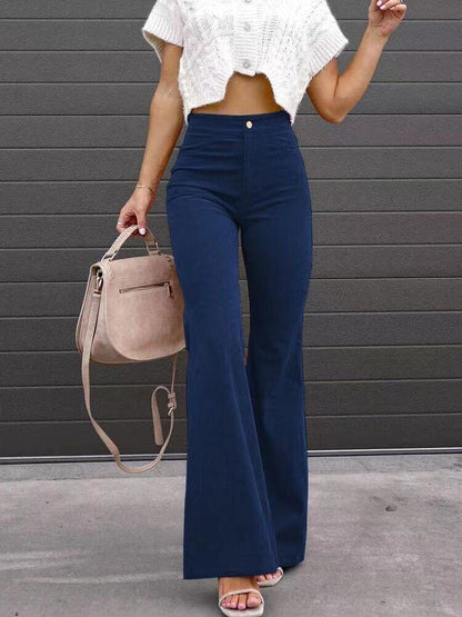 Full-body view of a woman wearing Harper high-waisted flare pants in a retro style, paired with a cropped top, holding a handbag, standing outdoors.