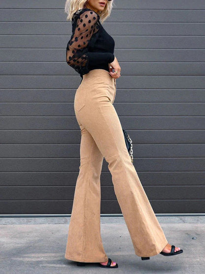 Full-body view of a woman wearing Harper high-waisted flare pants in a retro style, paired with a cropped top, holding a handbag, standing outdoors.