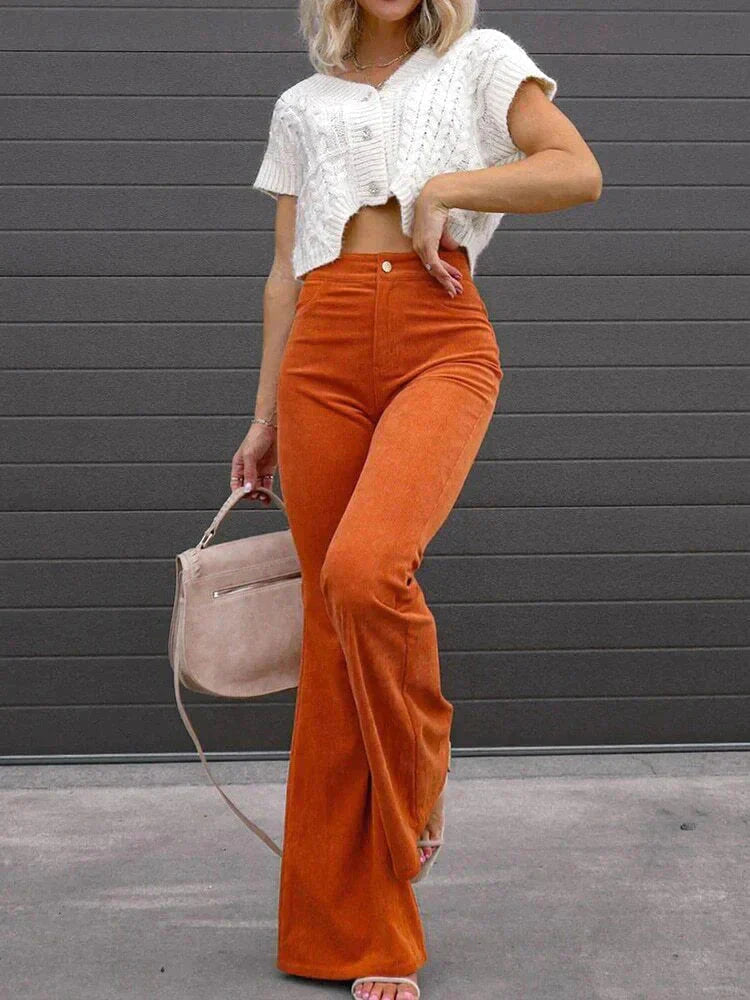 Full-body view of a woman wearing Harper high-waisted flare pants in a retro style, paired with a cropped top, holding a handbag, standing outdoors.