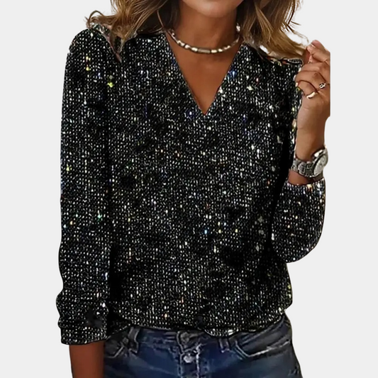 A woman wearing a sparkling V-neck top paired with denim jeans and accessorized with layered necklaces and a watch. The top features a glamorous design, perfect for parties, special occasions, or casual chic outfits.