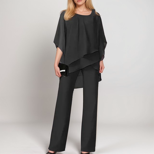 A stylish woman wearing the Sophia | Women's Layered Jumpsuit | Elegant Jumpsuit, featuring a flowing layered top and tailored wide-leg pants, accessorized with a clutch bag and heels, perfect for formal or special occasions.