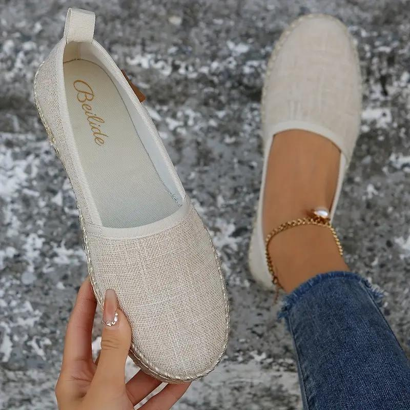 Close-up of a woman's hand holding a pair of slip-on shoes with a textured fabric design. One shoe is on her foot, showcasing a comfortable and casual style ideal for everyday wear.