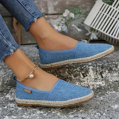 Close-up of a woman's hand holding a pair of slip-on shoes with a textured fabric design. One shoe is on her foot, showcasing a comfortable and casual style ideal for everyday wear.