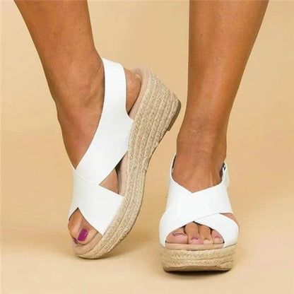 A close-up of a pair of Elena Women's Elegant Wedge Sandals being worn, featuring a stylish cross-strap design and a comfortable wedge sole. These sandals offer a blend of elegance and comfort, ideal for casual or dressy occasions.