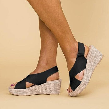 A close-up of a pair of Elena Women's Elegant Wedge Sandals being worn, featuring a stylish cross-strap design and a comfortable wedge sole. These sandals offer a blend of elegance and comfort, ideal for casual or dressy occasions.