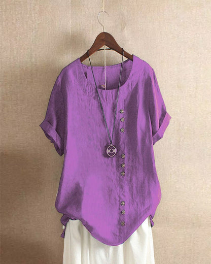 A casual women's blouse with an asymmetrical button design, short sleeves, and a relaxed fit, hanging on a wooden hanger. This blouse, part of the Mira collection, offers a unique style perfect for casual and everyday wear.